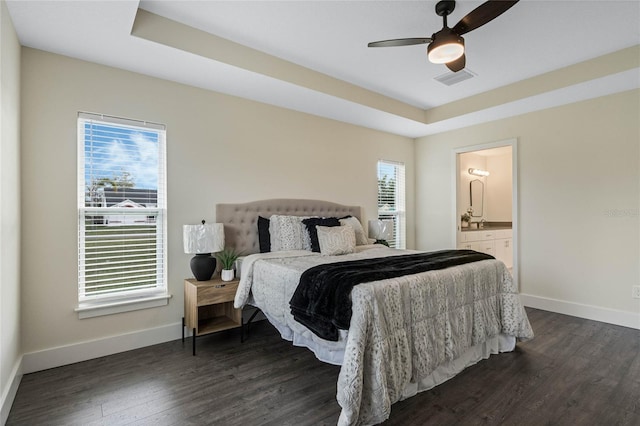 bedroom featuring ensuite bathroom, a tray ceiling, dark wood-style flooring, and baseboards