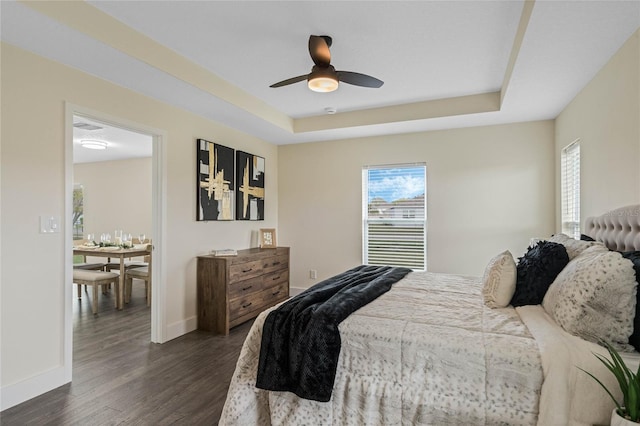 bedroom with a tray ceiling, multiple windows, dark wood finished floors, and baseboards