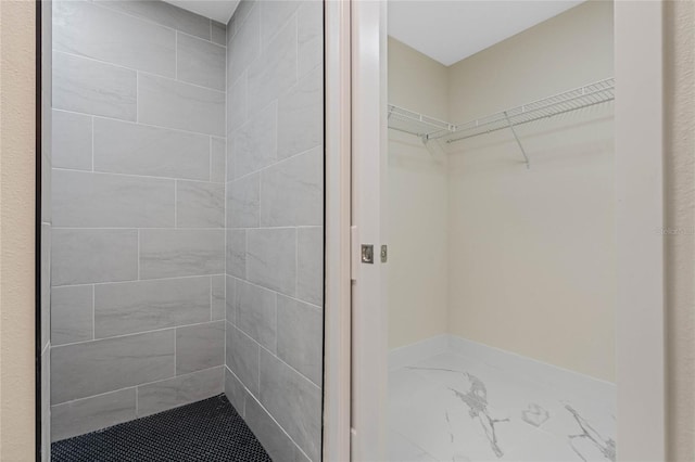 full bathroom featuring marble finish floor, tiled shower, and a walk in closet