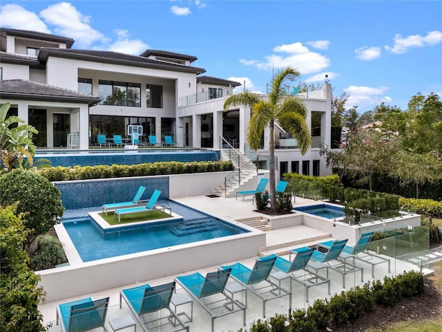 back of house featuring a hot tub, a balcony, stairway, a community pool, and a patio area