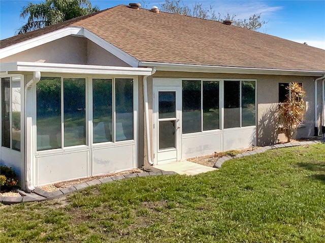 back of property featuring a sunroom, roof with shingles, a yard, and stucco siding