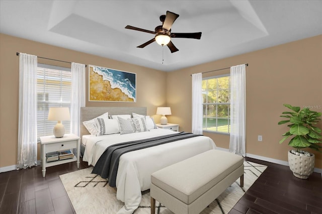 bedroom with a tray ceiling, baseboards, and dark wood-style flooring