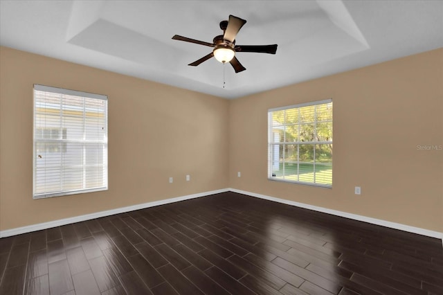 unfurnished room featuring ceiling fan, a raised ceiling, dark wood-type flooring, and baseboards