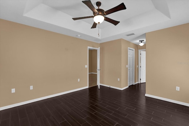 unfurnished room with a ceiling fan, wood finished floors, visible vents, baseboards, and a raised ceiling