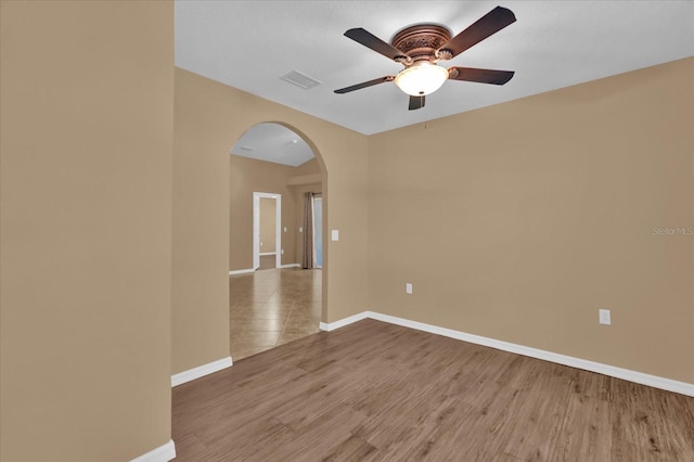 empty room featuring visible vents, wood finished floors, arched walkways, baseboards, and ceiling fan