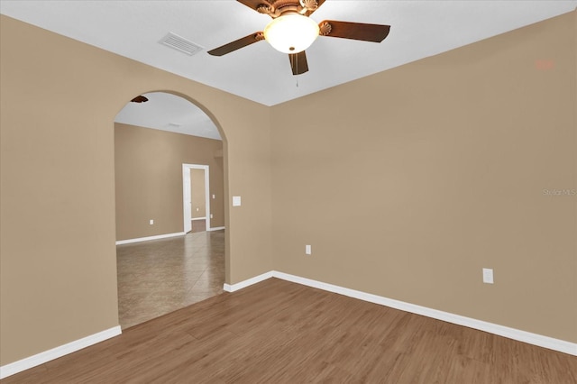 empty room with visible vents, arched walkways, baseboards, and wood finished floors