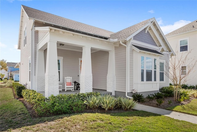 view of front of property featuring a porch, a shingled roof, and brick siding