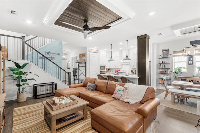 living area with light wood-type flooring, stairs, visible vents, and ceiling fan with notable chandelier