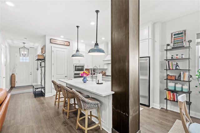 kitchen featuring built in appliances, a breakfast bar area, white cabinets, light countertops, and dark wood-style floors