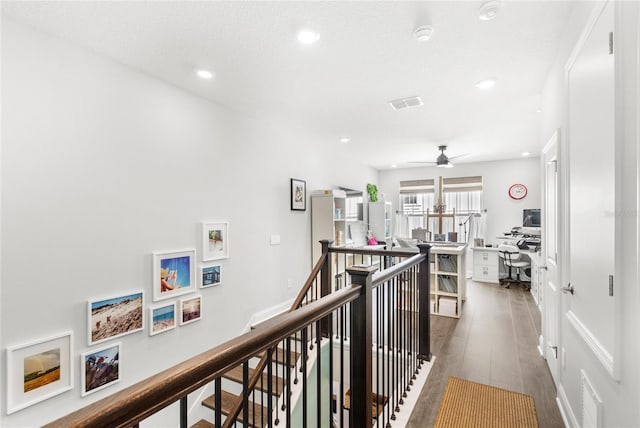 hall with recessed lighting, dark wood-type flooring, visible vents, baseboards, and an upstairs landing