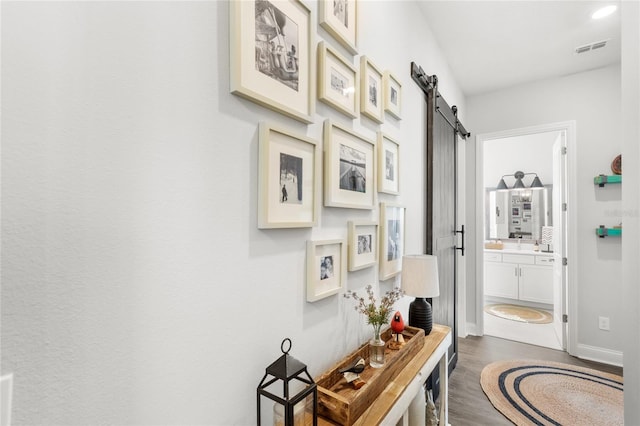 hall featuring a barn door, dark wood-style flooring, visible vents, and baseboards