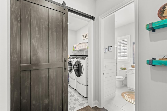 laundry area with laundry area, a barn door, wainscoting, washer and dryer, and light floors