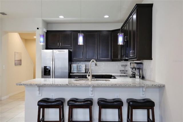 kitchen with light stone counters, stainless steel fridge, a sink, and backsplash