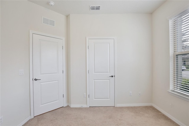 unfurnished bedroom featuring baseboards, visible vents, and light colored carpet