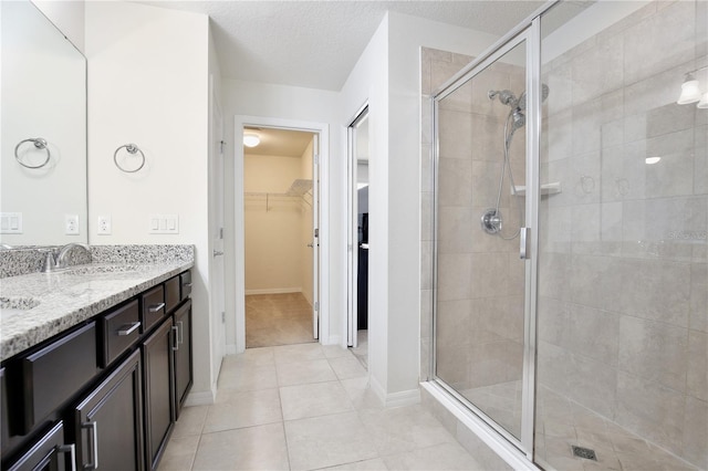 full bath featuring tile patterned floors, a spacious closet, a textured ceiling, a shower stall, and a sink