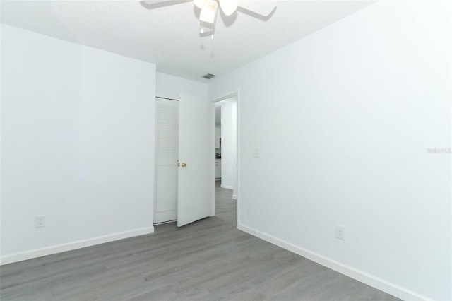 unfurnished bedroom with a closet, visible vents, a ceiling fan, wood finished floors, and baseboards