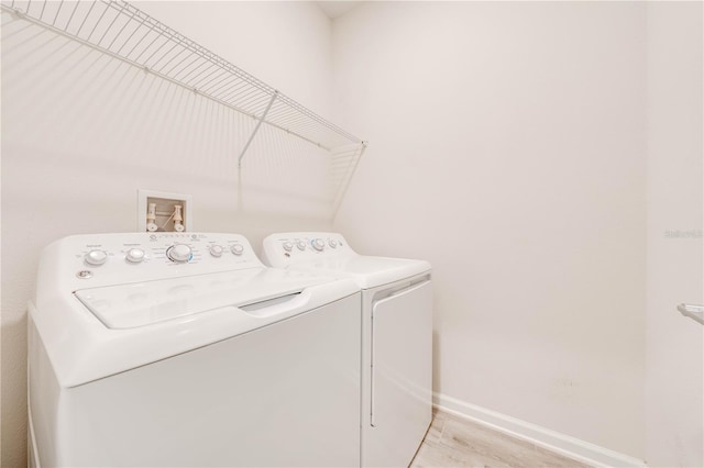 clothes washing area featuring light wood-type flooring, laundry area, washer and clothes dryer, and baseboards