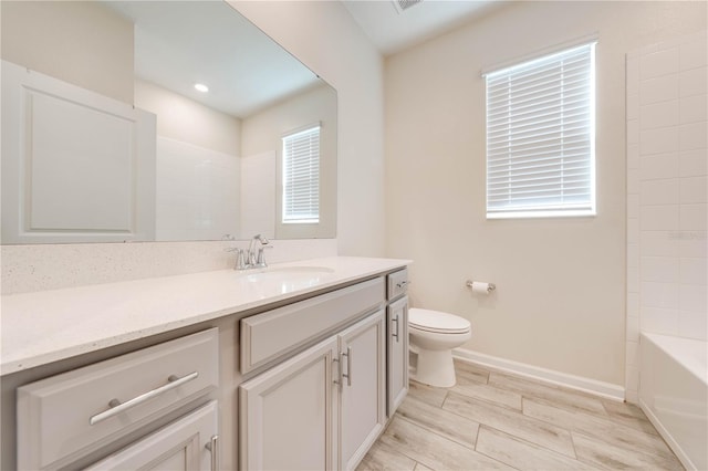 bathroom featuring toilet, plenty of natural light, baseboards, and vanity