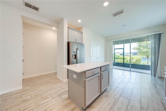 kitchen with wood tiled floor, stainless steel fridge, a kitchen island, and visible vents