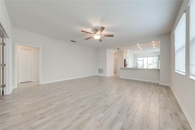 unfurnished living room featuring light wood-style floors, ceiling fan, visible vents, and baseboards