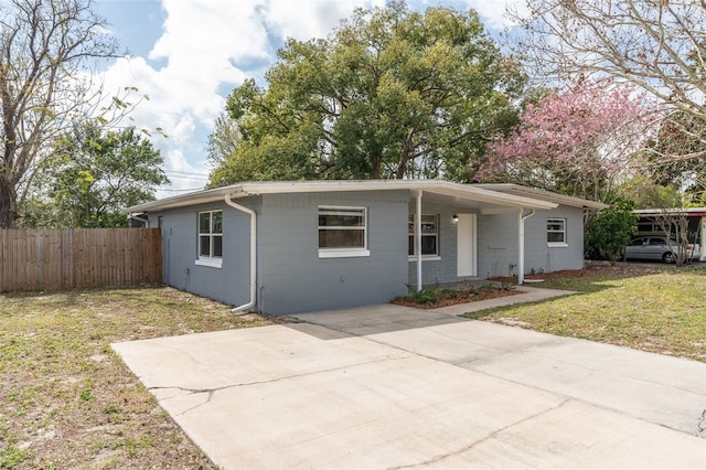 view of front of house featuring concrete block siding, concrete driveway, a front yard, and fence