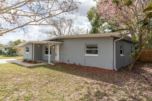 view of front of house with concrete block siding, a front yard, and fence