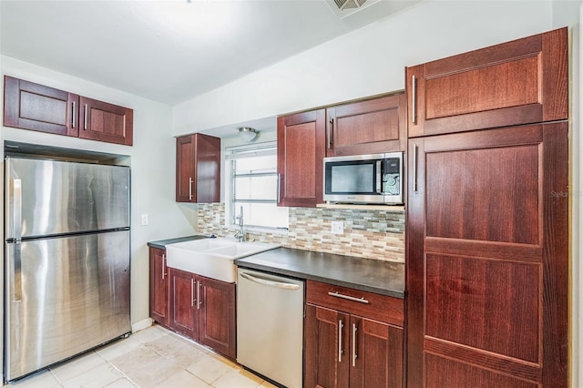 kitchen with a sink, tasteful backsplash, dark countertops, stainless steel appliances, and light tile patterned floors