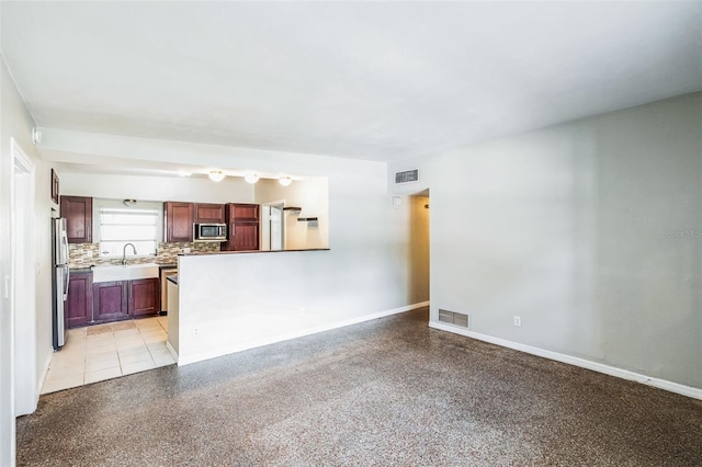 unfurnished living room featuring a sink, visible vents, baseboards, and light speckled floor