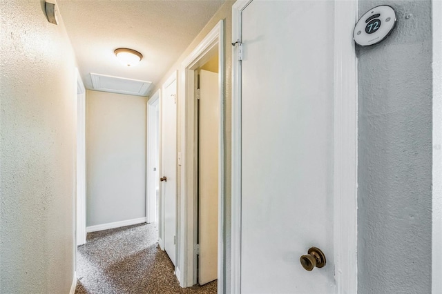 corridor with a textured ceiling, carpet, baseboards, attic access, and a textured wall