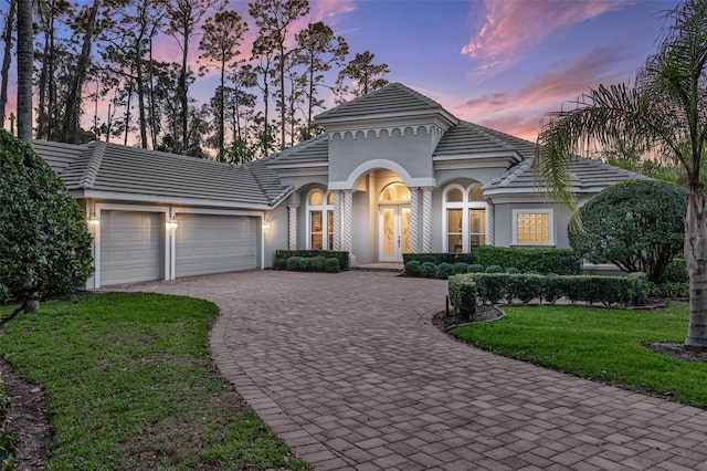 mediterranean / spanish home with an attached garage, a front lawn, decorative driveway, and stucco siding