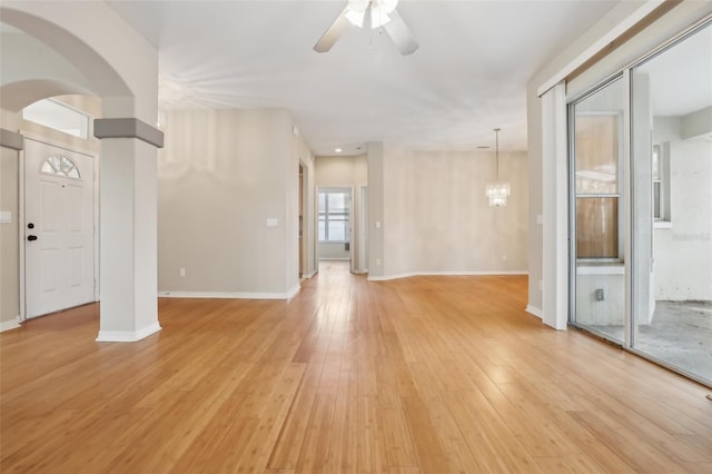 unfurnished living room featuring arched walkways, ceiling fan with notable chandelier, light wood-type flooring, and baseboards