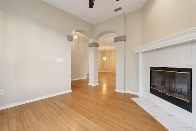 unfurnished living room with visible vents, ceiling fan, baseboards, a tile fireplace, and light wood-style floors