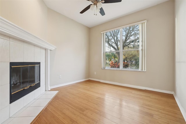 unfurnished living room featuring a tiled fireplace, light wood-style floors, baseboards, and ceiling fan