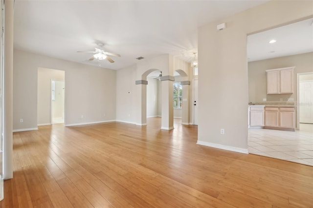 unfurnished living room featuring baseboards, arched walkways, light wood-style flooring, and a ceiling fan