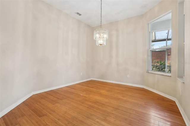 empty room featuring light wood-type flooring, visible vents, baseboards, and a chandelier