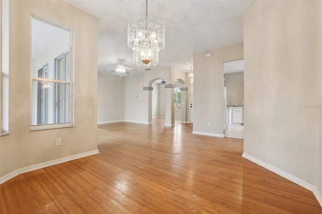 interior space featuring arched walkways, ceiling fan with notable chandelier, light wood-type flooring, and baseboards