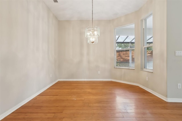 spare room with light wood-type flooring, baseboards, a notable chandelier, and visible vents