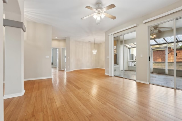 empty room featuring ceiling fan with notable chandelier, light wood-type flooring, and baseboards