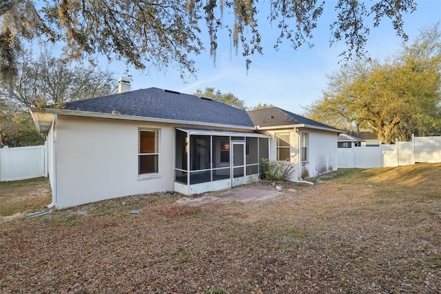 rear view of house with a lawn, a chimney, fence, and a sunroom