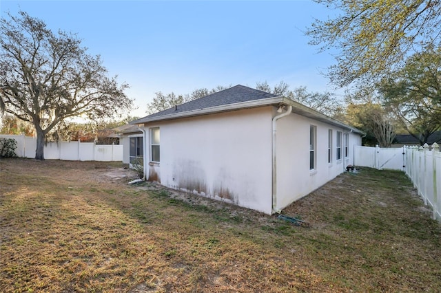 view of side of property featuring a yard, a shingled roof, a fenced backyard, and stucco siding