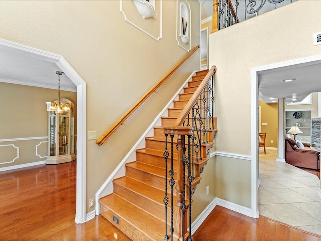 stairway with visible vents, baseboards, wood finished floors, an inviting chandelier, and crown molding