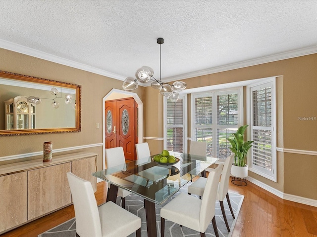 dining room with a textured ceiling, ornamental molding, wood finished floors, and baseboards