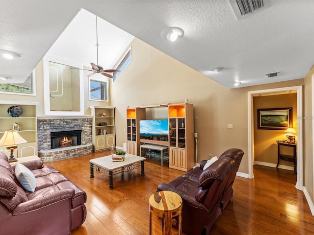 living area featuring baseboards, wood-type flooring, ceiling fan, a textured ceiling, and a fireplace