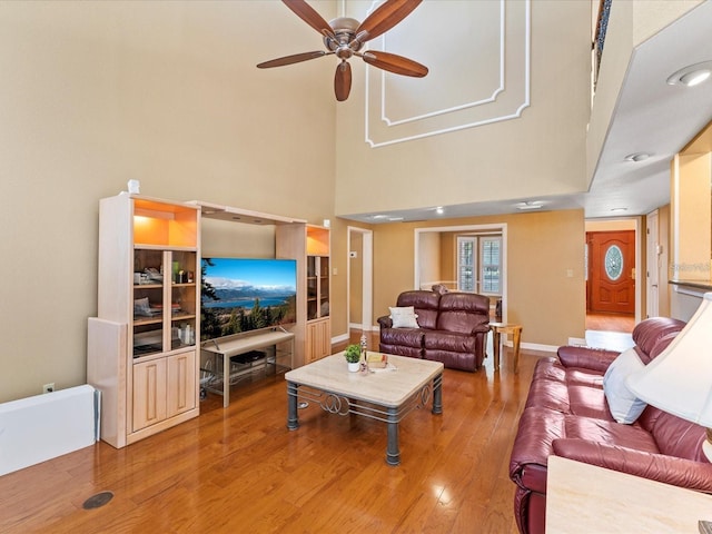 living room with ceiling fan, wood finished floors, a towering ceiling, and baseboards