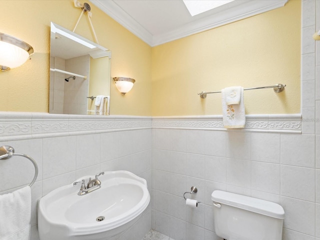 full bath featuring toilet, a wainscoted wall, a sink, ornamental molding, and a tile shower