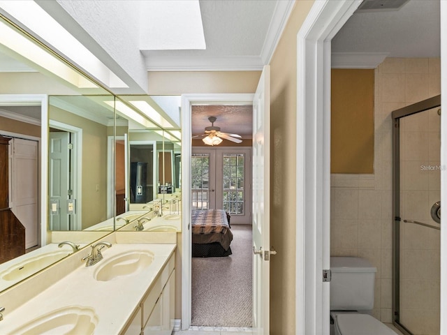 ensuite bathroom featuring a skylight, a shower stall, ornamental molding, and a sink