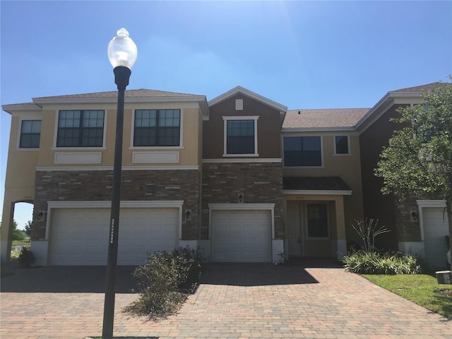 view of front of house featuring stone siding, decorative driveway, an attached garage, and stucco siding