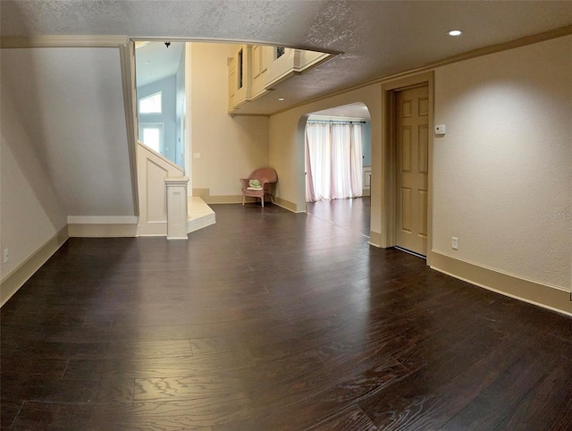 interior space featuring baseboards, arched walkways, dark wood-type flooring, a textured ceiling, and recessed lighting