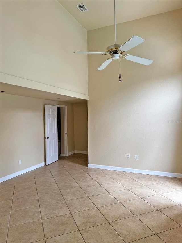 empty room with light tile patterned floors, visible vents, a towering ceiling, ceiling fan, and baseboards