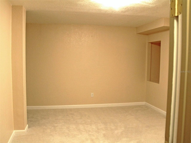 empty room with light carpet, a textured ceiling, and baseboards